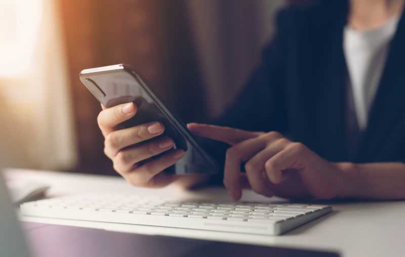 Person scrolling on their phone with keyboard underneath.