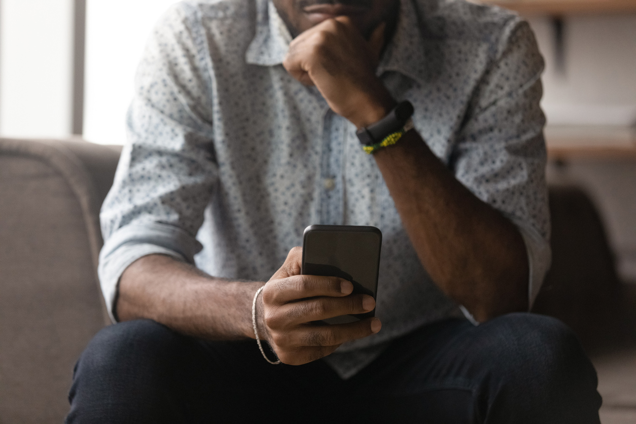 Cropped image thoughtful young African man using cellphone, feeling anxious getting spam scam message or email with bad news, dissatisfied with wrong device work, tech addiction concept.