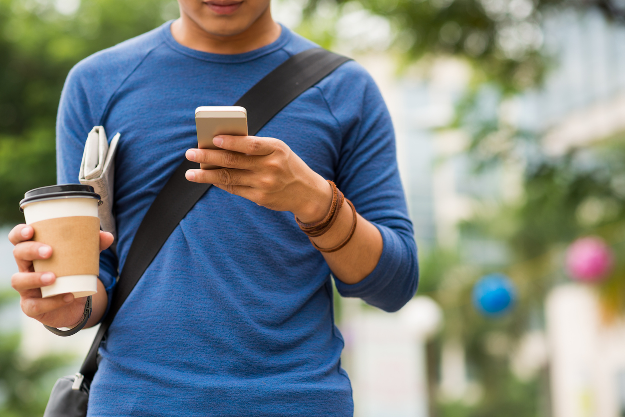 Man with take-out coffee and newspaper reading message on his phone