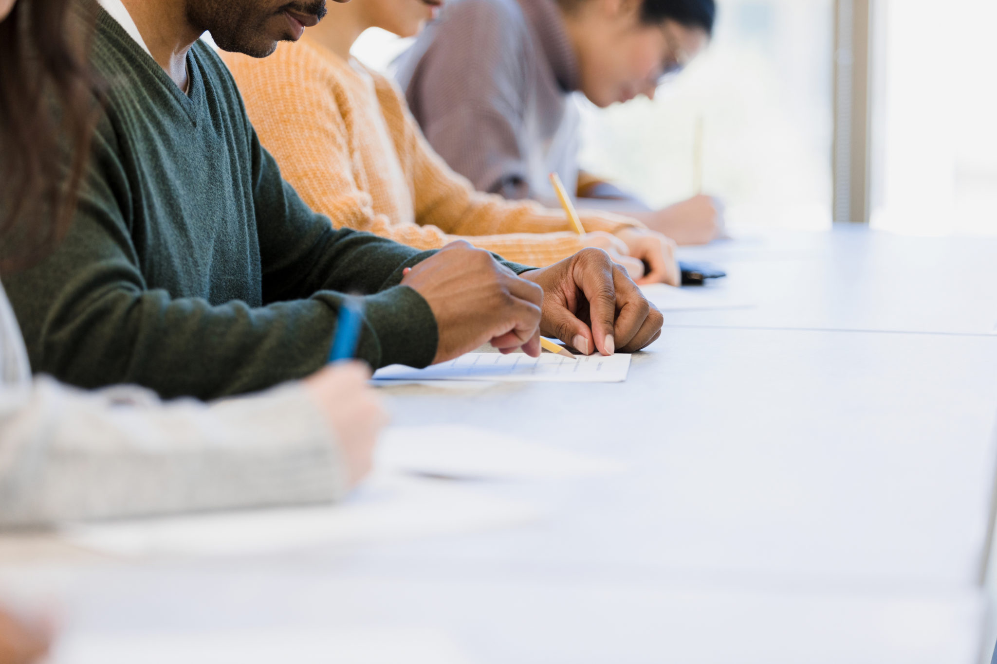 The group of unrecognizeable people work on an exam during class.