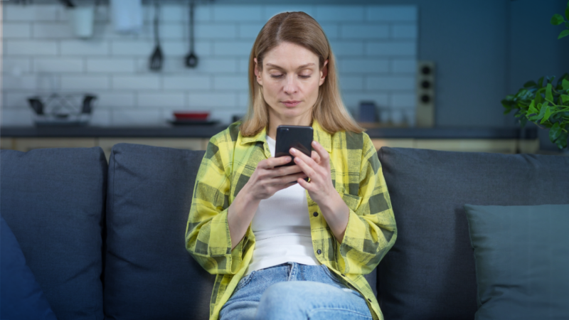 Woman sitting on a couch in her home using a mobile device to protect herself from cyber threats