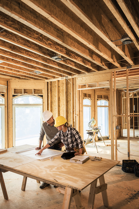 Woman architect looking over blueprints at home construction site.