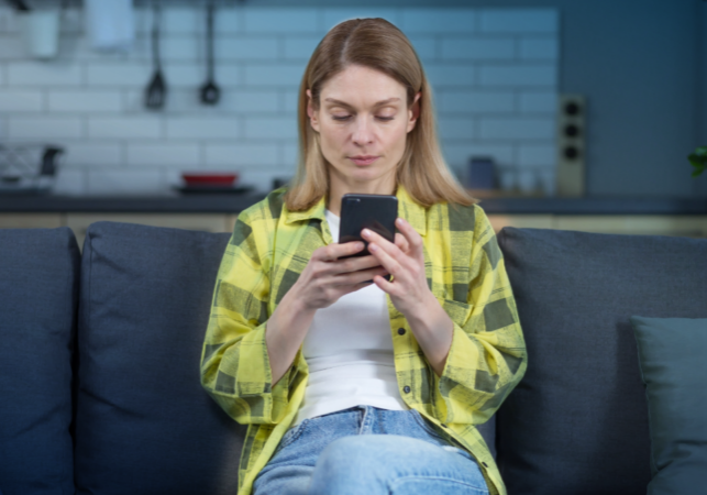 Woman sitting on a couch in her home using a mobile device to protect herself from cyber threats