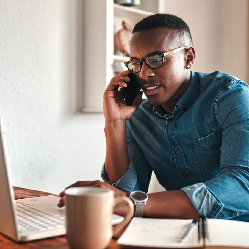 Cropped shot of a handsome young businessman sitting alone in his home office and talking on his cellphone