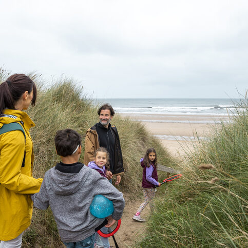 Caucasian parents with their young triplets walking to the beach in the North East of England. They are wearing warm clothing, carrying toys to play with, big rackets and balls.