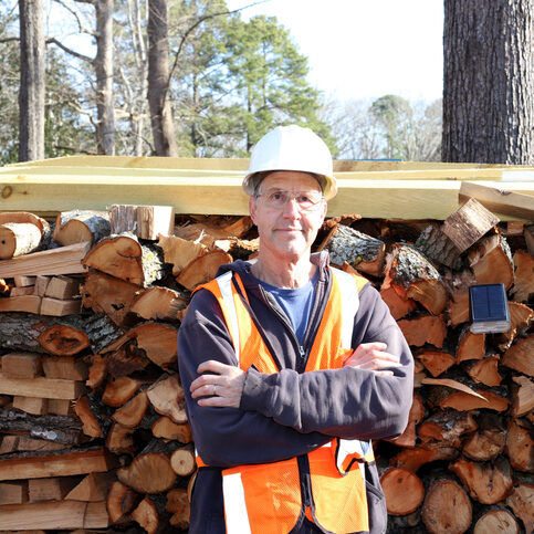 Man who works for a arborist stands in front of his stacks of wood.