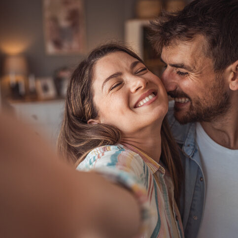 Beautiful couple taking selfie with smartphone in new apartment, smiling happy about new house